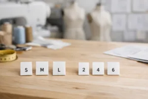 A workbench scene showing S/M/L and number sizing tags together illustrates the topic of Alpha Sizing (S/M/L) vs. Numeric Sizing (2, 4, 6): Pros and Cons.
