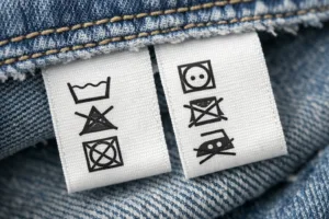 A crisp, macro photograph of care labels sewn onto denim, featuring common legal symbols and clear English text adhering to Care Label Requirements: Laws in US, UK, and EU.