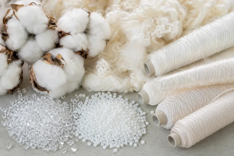 A high-resolution image showing raw samples of natural fibers (cotton bolls, wool) next to synthetic elements (polyester chips, nylon yarns) under bright, neutral lighting. Highlights material differences for natural vs. synthetic fibers.