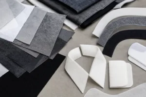 A clean studio flat lay showing different non-woven support materials used in apparel development.